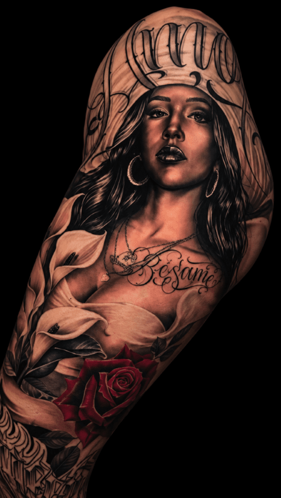 Black and grey chicana realism tattoo with lettering, calla lilies, and a rose, by Sergio Sanchez